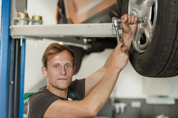 A young and handsome mechanic is trying to twist the wheel of a car for a tire service at a car workshop