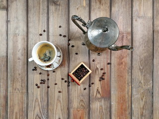 A cup of coffee with sugar, kettle and scattered coffee beans on wooden background. Flat lay photo of morning coffee in the village