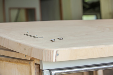 Two small steel screws and allen key on the edge of the wooden table that is situated in the carpenter workshop.