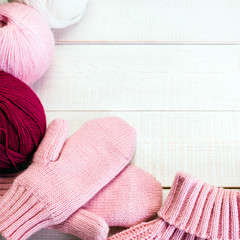 I love winter, knitted pink mittens on a white old wooden background, a skein of yarn
