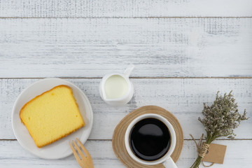 A cup of coffee, milk and butter cake with flower bouquet on white wood table with copy space