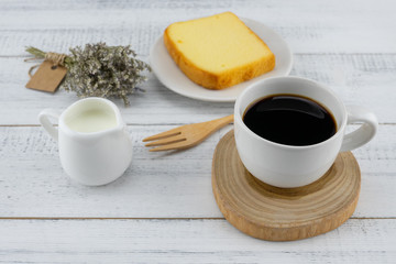 A cup of coffee, milk and butter cake with flower bouquet on white wood table, selective focus on coffee