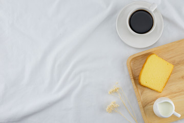 A cup of coffee, milk and butter cake with flower on wooden plate on white bed with copy space