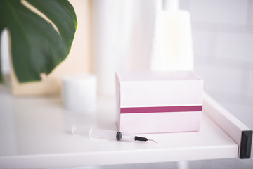 Perfect skincare. Close up of cardboard box with violet strip and needle. Cosmetics and personal care products on blurred background