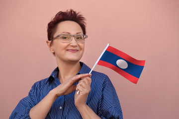 Laos flag. Woman holding Laos flag. Nice portrait of middle aged lady 40 50 years old with a national flag over pink wall background outdoors.