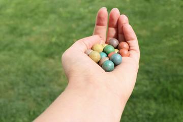 Small balls for playing marbles in hand of woman isolated on green bokeh background. 