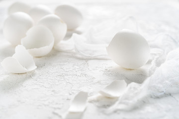 Broken eggshells of empty white eggs, scattered on white rustic background. Total white