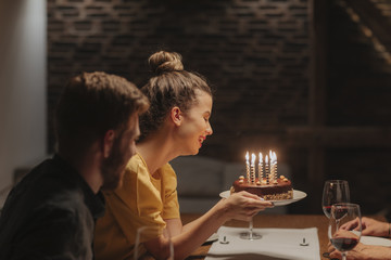 Beautiful smiling young woman holding birthday cake at party.