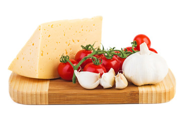 Wooden cutting board with fresh tomatoes, piece of cheese and garlic