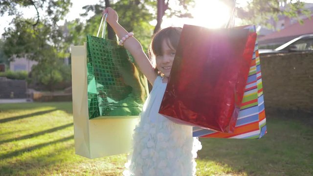 birthday, small girl buyer rejoices in gift into packages and raises hands up at park in sun rays