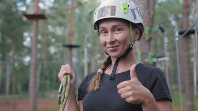 Young beautiful brunette overcomes obstacles in the rope town. A girl with a white helmet on her head and a rope in her hand shows like after passing the track