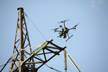 Quadcopter flying in a sky, electric pylon, cables and insulators on a background. July 10, 2018. Kiev, Ukraine