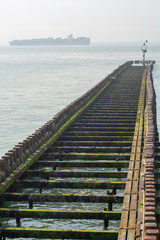 Fototapeta premium Sea near Vlissingen, Zeeland, Netherlands, old wooden pier at high tide and big cargo ship on horizon