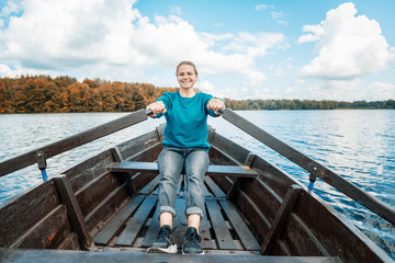 Young beautiful woman tourist traveler rowing oars on a wooden boat on the lake on a sunny day