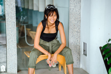 A sporty Asian woman wearing a very trendy tank top and cargo pants sits while she takes a break from exploring the city on a sunny day.