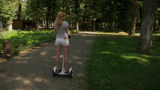 Girl in white shorts, riding a Segway on a clear sunny day. summer park and sun glare. 4k, slow-motion shooting, stadikam shot