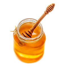 Wooden dipper with dripping honey and glass jar isolated on white background, macro