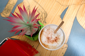 Freshly made, delicious coffee with milk and cinnamon on wooden table in cafe next to cactus plant.  
