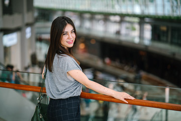 A young attractive Japanese tourist stands against the railing of a mall, overlooking a scenery...