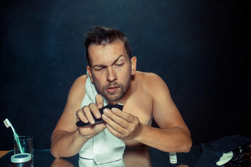 The young man in bedroom sitting in front of the mirror scratching his beard at home. Human emotions concept