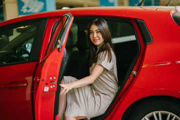 A young and attractive Japanese woman is alighting a red car which she booked from a ride hailing app. She is smiling happily as she excitedly reaches her destination.