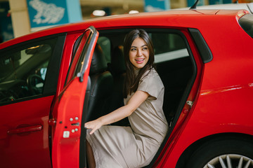 A young and attractive Japanese woman is alighting a red car which she booked from a ride hailing app. She is smiling happily as she excitedly reaches her destination.