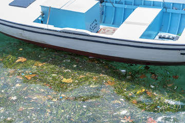 Old Wooden fishing boat with white hull closeup and sea ​​pollution