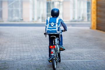 Schoolkid boy in safety helmet riding with bike in the city with backpack. Happy child in colorful...