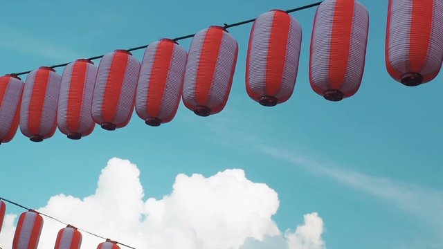 Paper red-white japanese lanterns Chochin hanging on blue cloudy sky background