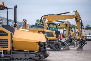 Multiple cars, excavators, trucks, loaders, concrete mixers and construction machinery in large parking lot in industrial territory, next to concrete and asphalt factory 