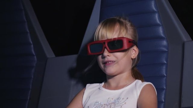 The girl is watching a movie in a movie theater with special effects. The armchair moves, glasses are put on it