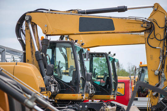 Multiple cars, excavators, trucks, loaders, concrete mixers and construction machinery in large parking lot in industrial territory, next to concrete and asphalt factory 