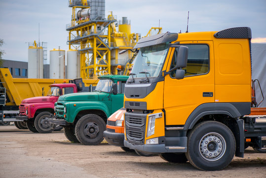Multiple cars, trucks, loaders, concrete mixers and construction machinery in large parking lot in industrial territory, next to concrete and asphalt factory   
