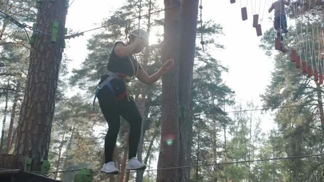 Young beautiful brunette overcomes obstacles in the rope town. A girl with a white helmet on her head and protective gear is on the track