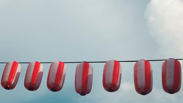 Paper red-white japanese lanterns Chochin hanging on blue cloudy sky background
