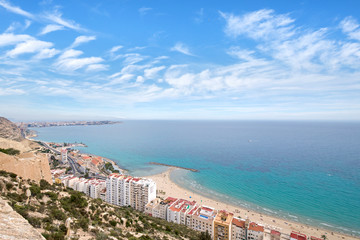 Panoramic view of Postiguet beach  from Santa Barbara Castle in Alicante, Spain. Sunny day at Mediterranean sea. Block apartment buildings in a row. Palm trees and vibrant blue water.