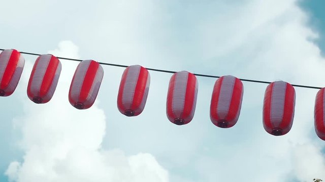 Paper red-white japanese lanterns Chochin hanging on blue cloudy sky background