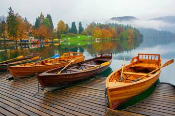 Fototapeta premium Autumn scenery with boats moored on Bled lake at foggy day