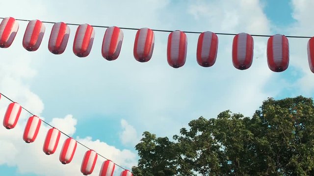 Paper red-white japanese lanterns Chochin hanging on blue sky background and trees