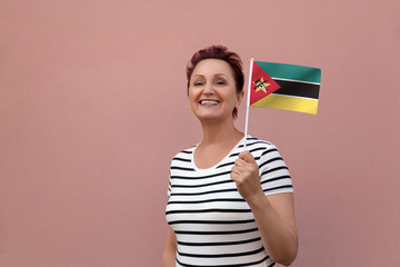 Mozambique flag. Woman holding Mozambique flag. Nice portrait of middle aged lady 40 50 years old with a national flag over pink wall background outdoors.