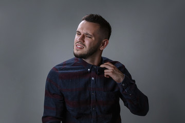 Tired young bearded man taking off collar, removing his tie on dark grey background