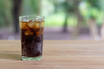 Refreshing black soda soft drinks or cola with ice in a clear tall glass with nature background.