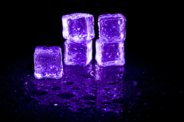 Purple ice cubes reflection on black table background.