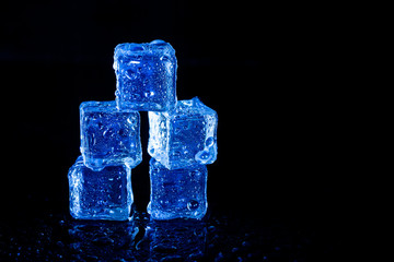 Blue ice cubes reflection on black table background.