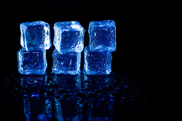 Blue ice cubes reflection on black table background.