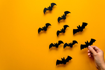 Woman's hand holding bat and black paper bats flying on yellow background. Halloween concept. Paper cut style. Top view