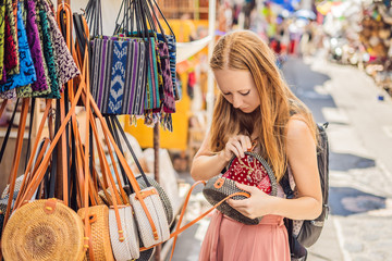 Shopping on Bali. Young woman chooses Famous Balinese rattan eco bags in a local souvenir market in...