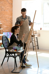 Male teacher helping his student during classes in school of painters