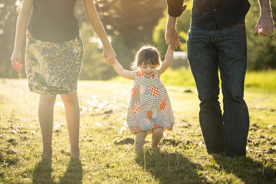 Little girl wearing a dress gets a swing from her parents while holding their hands.