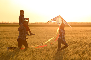 Fototapeta na wymiar Happy family flying kite in the field at sunset